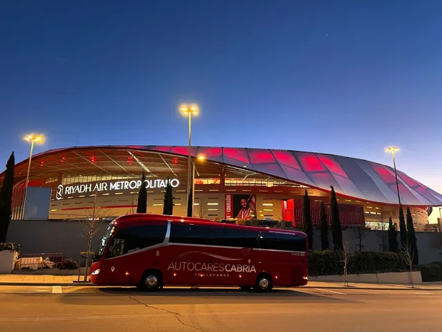 Autocar de Autocares Cabria frente a un estadio iluminado de rojo
